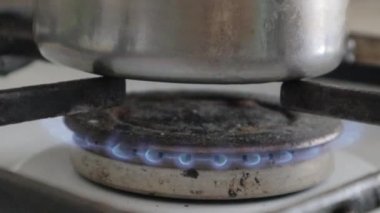 Tencereyi yakın çekim ateşe verdi. Gaz ocağında tencerede yemek pişirmek. Mutfak ocağında yemek pişirmek için gaz ocağı var. Yanan propan ateşiyle mutfak gaz ocağı. Doğal gaz kavramı.