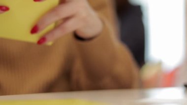 Tanınmayan bir kadın küçük sarı bir karton kutuyu katlıyor. Kağıttan karton kutu üretimi. Ambalaj imalat şirketi. Yaratıcı bir derste kağıt işçiliği yapan ellerin yakın çekimi..