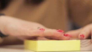 Tanınmayan bir kadın küçük sarı bir karton kutuyu katlıyor. Kağıttan karton kutu üretimi. Ambalaj imalat şirketi. Yaratıcı bir derste kağıt işçiliği yapan ellerin yakın çekimi..