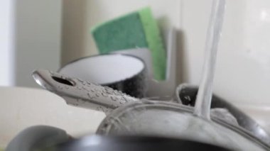 Lavabodaki mutfak aletlerinin yıkanması gerekiyor. Mutfak lavabosunda akan suyla birlikte bir yığın kirli bulaşık. Mutfak aletlerinin yıkanması gerekiyor. Ödev konsepti.