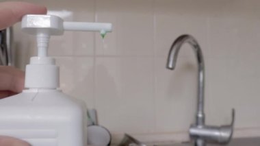 Bir adamın eli bulaşık deterjanını bulaşık ve mutfak gereçleriyle dolu kirli bir lavaboya bastırır. Mutfakta bulaşık deterjan ve süngerle elle yıkılıyor..