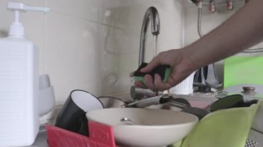 El süngeri köpükle sıkar. Bir adamın eli makineye basar ve kirli ve yağlı bulaşıkları yıkamak için yeşil bir süngerin üzerindeki sıvı deterjanı çeker, yakın plan. Tipik mutfak rutini..