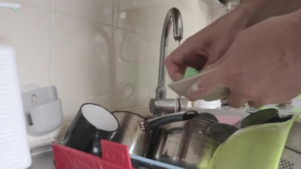 クローズアップ男性の手は 泡の洗濯布で台所のシンクで汚れて脂っこいプレートを洗浄します 石鹸泡と泡 緑色のスポンジで皿をきれいにしてきれいにする — ストック動画