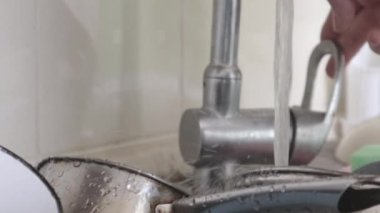 Mutfak lavabosunun kapağı suyu kapatıyor. Erkeklerin elleri bir sürü bulaşığı yeşil bir süngerle yıkadı ve musluğu kapattı. Püskürt. Düşen su damlaları. Kapat.