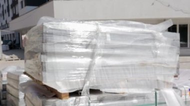 Tahta standart taşıma paleti üzerine döşenmiş kaldırım taşları olan bir inşaat alanı. Paletlerin üzerinde fayanslar var. Paketleme ürünleri. Kodec Prores. Paletlerin üzerinde uzanan yeni taşlar.