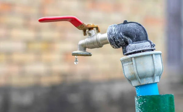 Water faucet on the background of nature. Opening or closing a faucet to save water indicates a water shortage problem. Rustic fountain with daylight. Selective focus with blurred background