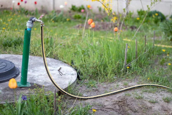 Plumbing, water pump from a well. An outside water faucet with a yellow garden hose attached to it. Irrigation water pumping system for agriculture. Hose in the garden for watering, sunny summer day