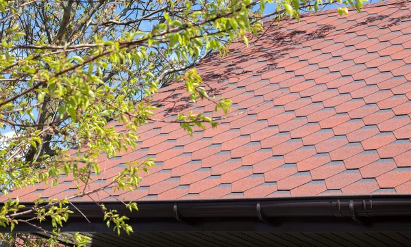 New roof with red shingles against the blue sky. High quality photo. Tiles on the roof of the house. Use to advertise roof fabrication and maintenance. Spotted texture. Affordable roofing