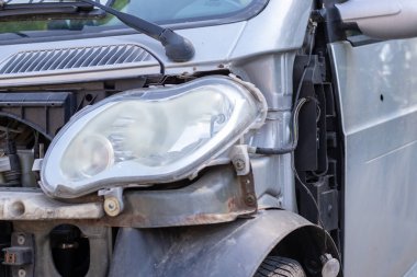 Çarpışma sonucu kırık farlar var. Kazadan sonra kırık gri bir araba. Araba kazası konsepti. Hasarlı acil durum farları, kaput ve tampon. Kazadan sonra cesette hasar var.