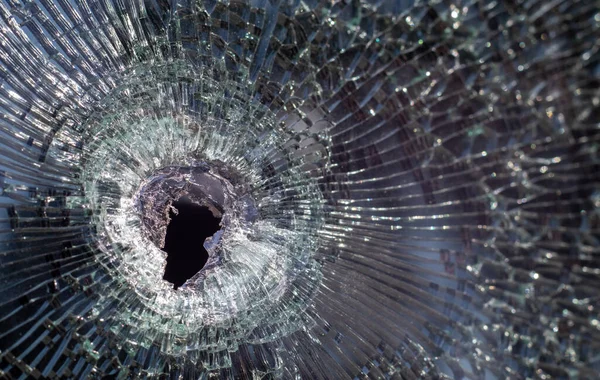 Bullet hole in glass with cracks, real bullet hole close-up. Authentic shot. The bullet made a cracked hole in the windshield of a car or a window glass shattered as a result of an accident