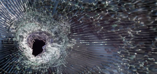 Bullet hole in glass with cracks, real bullet hole close-up. The bullet made a cracked hole in the windshield of a car or a window glass shattered as a result of an accident. Banner with copy space