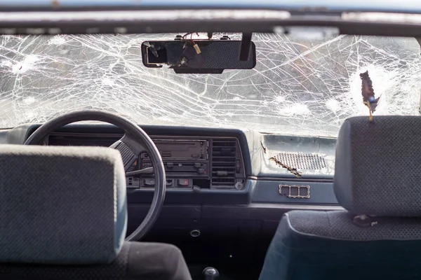 Broken windshield of a car from a bullet, from a shot from a firearm, view from the inside of the cabin. Damaged glass with traces of an oncoming stone on the road. Interior view of the car