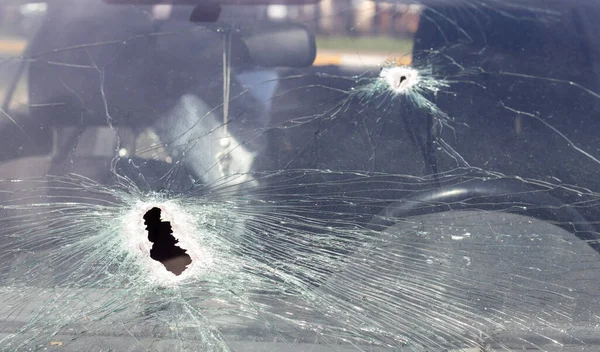 Holes on the windshield of the car, it was shot from a firearm. Bullet holes. Smash car windshield, broken and damaged car. The bullet made a cracked hole in the glass