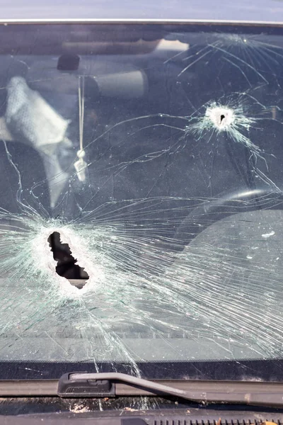 Holes on the windshield of the car, it was shot from a firearm. Bullet holes. Smash car windshield, broken and damaged car. The bullet made a cracked hole in the glass