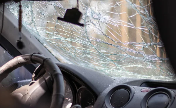 Broken windshield of a car from a bullet, from a shot from a firearm, view from the inside of the cabin. Damaged glass with traces of an oncoming stone on the road. Interior view of the car