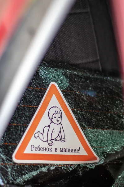 Warning sign of children inside a car after an accident with bloody broken glass. Translation: Child in the car. Close-up of white baby on board sticker on car back window. Vertical photo