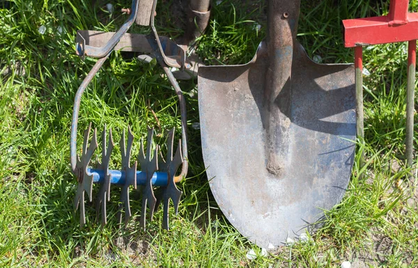 Gardening tools. Garden tools on the background of a garden in green grass. Summer work tool. Shovel, fork and baking powder stacked in the garden outside. The concept of gardening tools