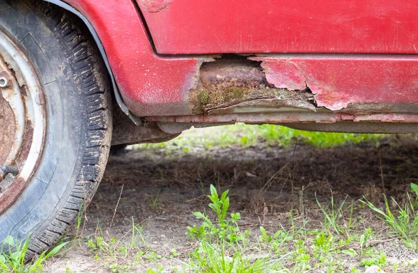 Rusty driver\'s door sills. Corrosion of the body of a red old car after winter. Influence of reagents in winter on an unprotected vehicle body. Damage to the left side, rotten threshold on the bottom