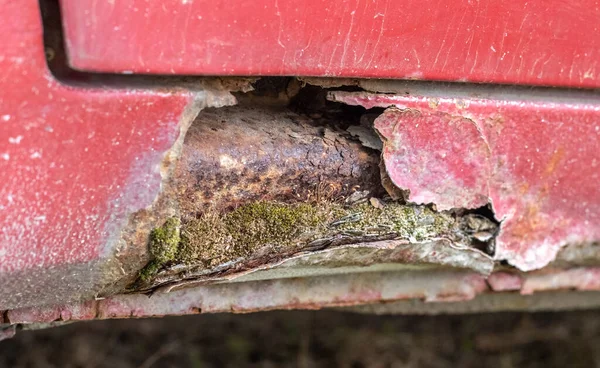 Rusty driver\'s door sills. Corrosion of the body of a red old car after winter. Influence of reagents in winter on an unprotected vehicle body. Damage to the left side, rotten threshold on the bottom