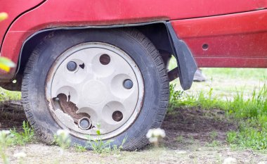 Çamur ve kir içinde yıpranmış araba tekerleği. Paslı terk edilmiş araba otoparkta. Eski bir arabanın restorasyonu. Lastik patladı. Klasik kırmızı araba şapkalı klasik tekerlek.