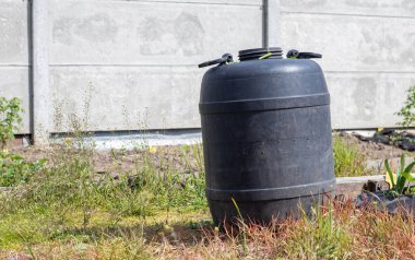 Yaz bahçesinde su bulunan büyük siyah plastik fıçı. Bahçede yağmur suyu tankı, sıcak yaz günü. Bahçeyi sulamak için fıçılar.
