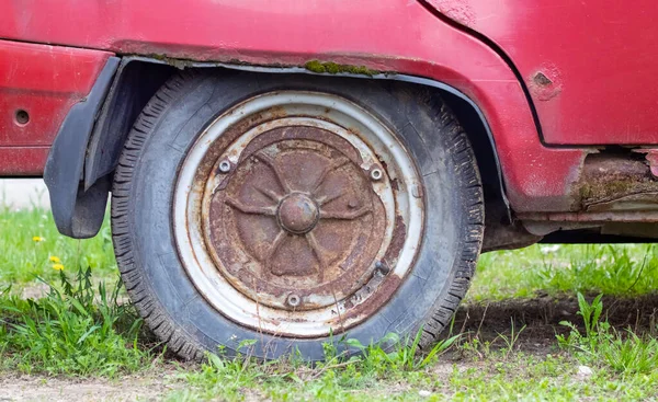 Weathered car wheel with dirt and grime. Rusty abandoned car in the parking lot. Restoration of a retro car. Flat tire. Vintage wheel with classic red car cap