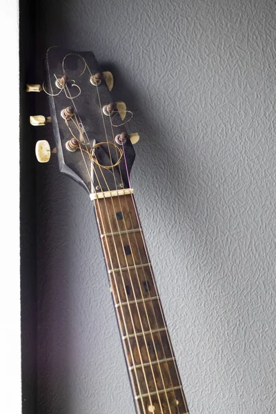 An acoustic old guitar in dust stands against a gray wall with copy space. Background for a screensaver with a musical instrument in the old style. Vertical photography