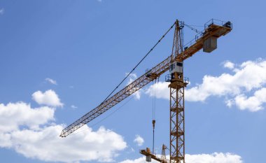 Güneşli bir günde bulutlu bir gökyüzüne karşı çalışan bir vinç. Kentsel gelişim ve inşaat kavramı. Endüstriyel geçmiş. Turna mühendisliği, inşaat endüstrisi aracı
