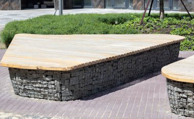 İçinde taşlar olan Gabion sepetlerinden ahşap banklar. Eldivenlere tahta monte edilmiş. Modern tasarımın sıraları. Bir dinlenme alanı var. Alçak Gabion duvarının, ahşap kapaklı ayrıntıları.