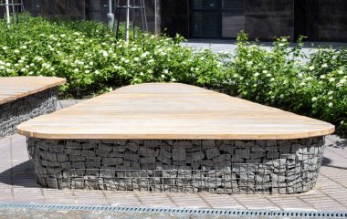 İçinde taşlar olan Gabion sepetlerinden ahşap banklar. Eldivenlere tahta monte edilmiş. Modern tasarımın sıraları. Bir bank olarak kullanmak için düşük ahşap kaplama Gabion duvarının ayrıntıları