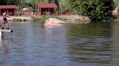 Deneyimli bir wakeboardcu sıçrama yapıyor. Kablolu yayın parkındaki gölde uyanış sırasında sporcu. Extreme Wakeboardcu su parkında numaralar yapıyor. Ukrayna, Kyiv - 07 Ağustos 2022.