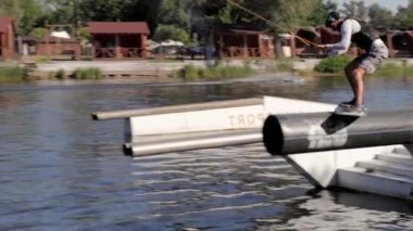 Deneyimli bir wakeboardcu sıçrama yapıyor. Kablolu yayın parkındaki gölde uyanış sırasında sporcu. Extreme Wakeboardcu su parkında numaralar yapıyor. Ukrayna, Kyiv - 07 Ağustos 2022.