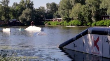 Deneyimli bir wakeboardcu sıçrama yapıyor. Kablolu yayın parkındaki gölde uyanış sırasında sporcu. Extreme Wakeboardcu su parkında numaralar yapıyor. Ukrayna, Kyiv - 07 Ağustos 2022.