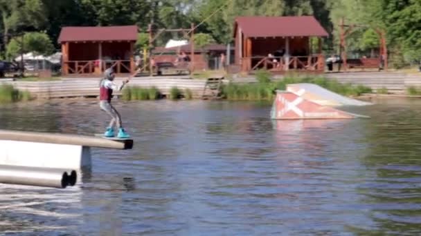 経験豊富なウェイクボーダーがジャンプします ケーブルウェイクパークで湖でのウェイクサーフィン中のアスリート ウォーターパークでトリックを実行する極端なウェイクボード ウクライナ キエフ 2022年8月7日 — ストック動画