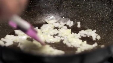 Bir tavada doğranmış soğan. Kızarmış soğan, kalori, sağlık sigortası ve zarar. Şef soğanı gaz sobasında tavada kızartıyor, yanmasın diye karıştırıyor.