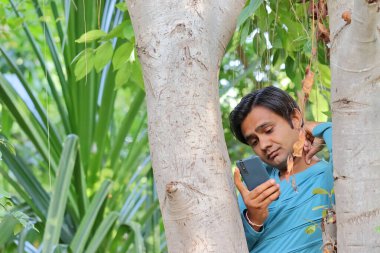 Bahçedeki cep telefonuna bakan yakışıklı bir çocuğun yakın plan fotoğrafı.