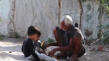 Pali Rajasthan, Hindistan. 17 Mart 2021. Yakın çekimde küçük çocuklar ya da küçük torunlar Hindistan 'da yaşlı bir büyükbabayla ağaçların yaprakları ve yerde oynuyorlar.