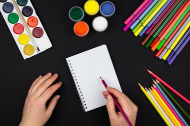 Kız not defterine not alıyor, siyah arka plandaki kalem ve resimlerin yanına.