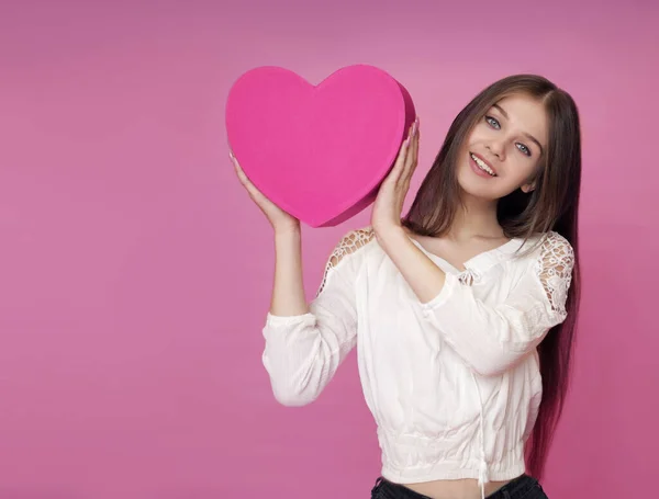 Linda chica sosteniendo un corazón en sus manos sobre un fondo rosa —  Fotos de Stock