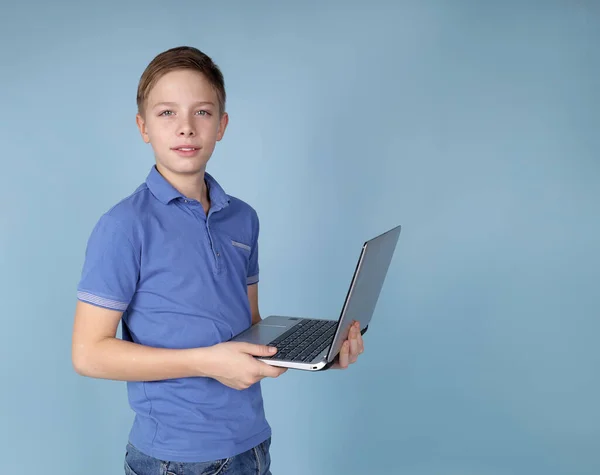 Lindo chico sosteniendo un portátil de pie sobre un fondo azul. — Foto de Stock