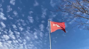 Mavi gökyüzü ve beyaz bulutlarla dolu rüzgarlı bir günde İsviçre bayrağı. Yüksek açı görünümü.