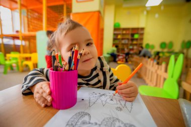 Çocuk oyun odasındaki bir çocuk masaya kalemlerle resim çizer.