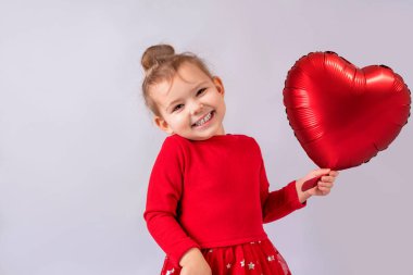 Küçük kız elinde şişme kalp şeklinde bir balonla gülümsüyor.