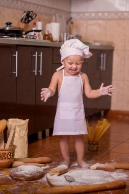 Çocuk yerde un ve ekmekle oynuyor. Aşçı gibi giyinmiş.
