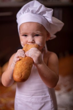 Çocuk yerde un ve ekmekle oynuyor. Aşçı gibi giyinmiş.