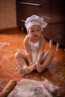 Çocuk yerde un ve ekmekle oynuyor. Aşçı gibi giyinmiş.