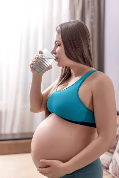 Ciężarna kobieta w odzieży sportowej pije wodę — Zdjęcie stockowe