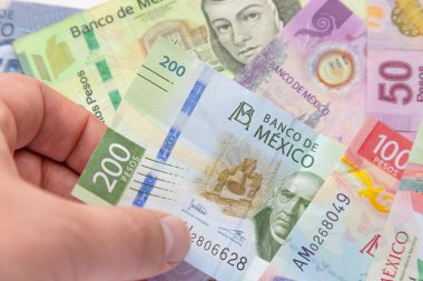 Arka planda daha fazla fatura olan iki yüz Meksika banknotu tutan bir kişi. Kavram: Enflasyon