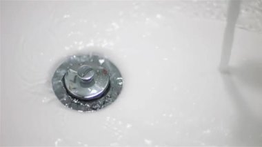 Durdurucu conta ile beyaz bir lavaboda temiz suyun yavaş akışı..