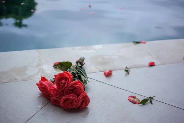 Разбросанные лепестки изношенного букета роз у бассейна — стоковое фото